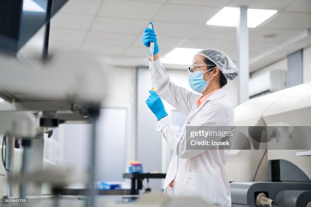 Vista lateral da cientista mulher pipetando produto químico em tubo de ensaio em laboratório