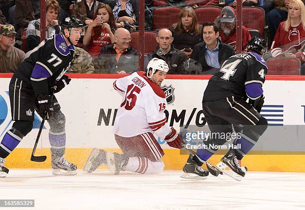 Boyd Gordon of the Phoenix Coyotes looks to pass the puck from his knees between Jeff Carter and Davis Drewiske of the Los Angeles Kings during the...