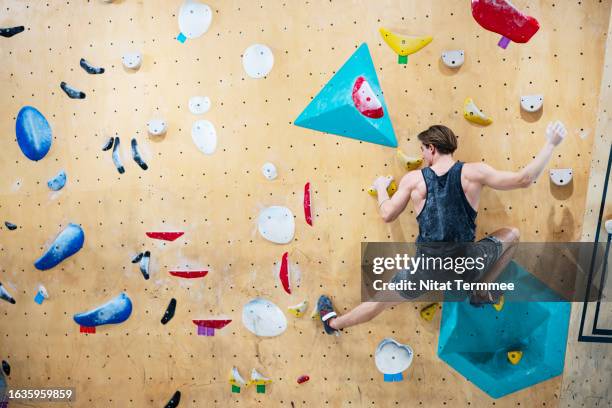 starting indoor rock climbing is a thrill and really good for you to increase mental and physical health. rear view of a male climber climbing up on a bouldering wall in an indoor rock climbing gym. - parete rocciosa foto e immagini stock