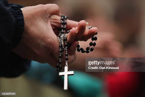 Woman holds rosary beads while she prays and waits for smoke to emanate from the chimney on the roof of the Sistine Chapel which will indicate...