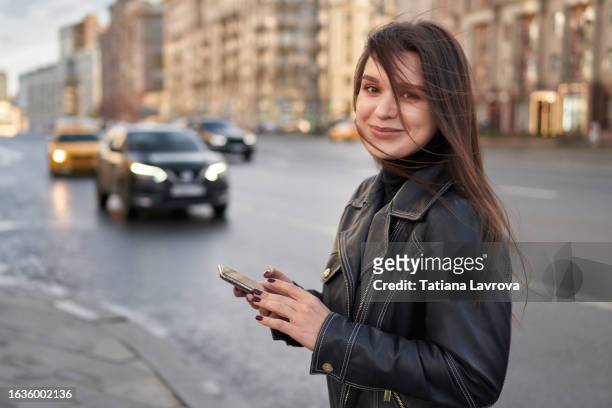 attractive young female millennial generation in the street. portrait of a woman waiting for a taxi on a windy autumn day. lifestyle photo with copy space - air taxi stock pictures, royalty-free photos & images