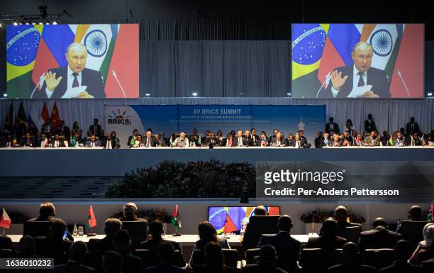 Delegates look on as Russian President Vladimir Putin delivers a speech at a meeting during the closing day of the BRICS summit at the Sandton...