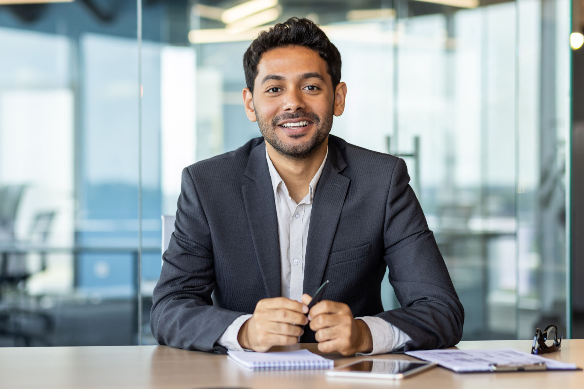 Portrait of young hispanic businessman inside office, boss in business suit smiling and looking at camera, experienced satisfied man at workplace at desk Portrait of young hispanic businessman inside office, boss in business suit smiling and looking at camera, experienced satisfied man at workplace at desk
