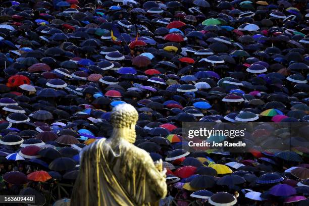 Statue of St Peter looks down upon people sheltering from the rain under umbrellas as they gather in St Peter's Square as they wait for news on the...
