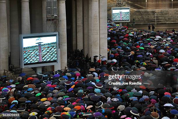 People gather around television screens in St. Peters Square displaying footage of the chimney on the roof of the Sistine Chapel as people wait for a...