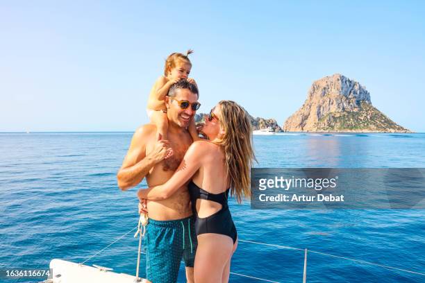 happy family with father carrying baby girl on shoulders laughing during vacations sailing on private catamaran deck on ibiza island. - es vedra stock pictures, royalty-free photos & images