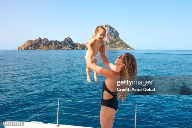 mother playing raising a baby girl during vacations sailing on private catamaran deck on ibiza island. - es vedra stock pictures, royalty-free photos & images