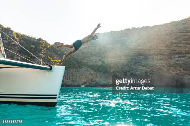 man diving into water headlong from a catamaran sailing in the ibiza island. - angel island stock pictures, royalty-free photos & images