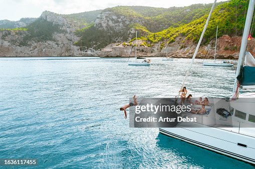 A group of friends relaxing and diving into water from the catamaran bow during luxury vacations in the Ibiza island. A group of friends relaxing and diving into water from the catamaran bow during luxury vacations in the Ibiza island.