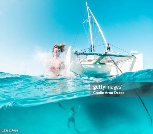 half underwater view of a woman jumping from the catamaran bow anchored in the mediterranean sea. - isole baleari foto e immagini stock