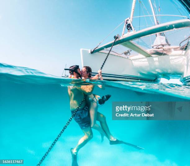 creative picture half underwater view of a couple kissing under the catamaran in the mediterranean sea. - travel fotografías e imágenes de stock