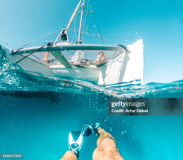 half underwater view of guy snorkeling from a personal perspective under catamaran during vacations. - perspectiva personal fotografías e imágenes de stock