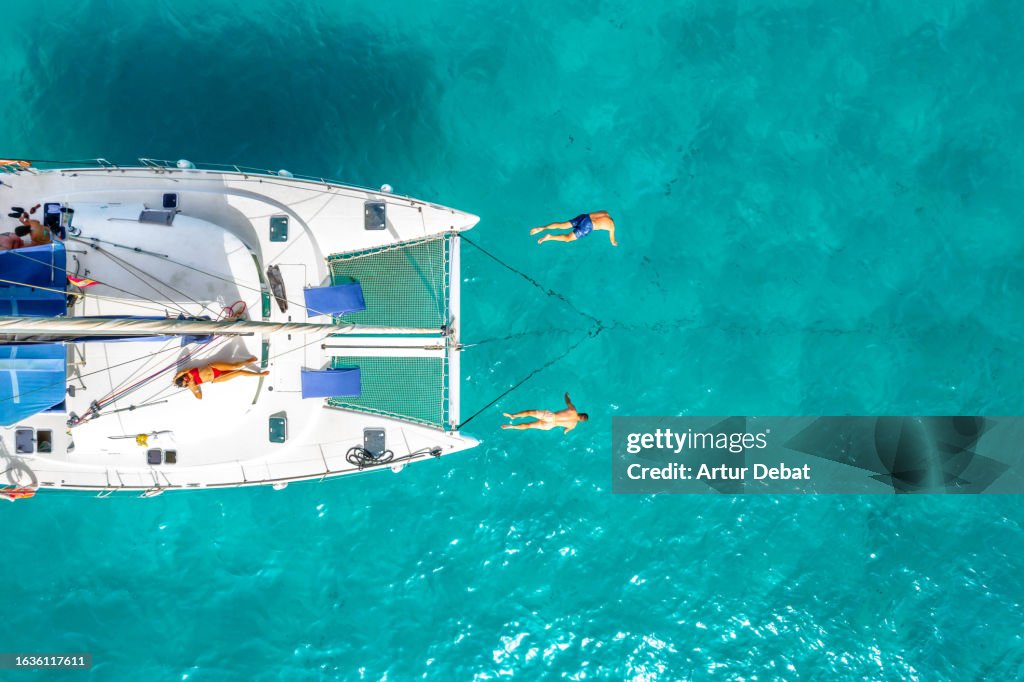 Directly above view of a group of friends jumping headlong from a catamaran during sailing vacations in the Formentera island of Spain.