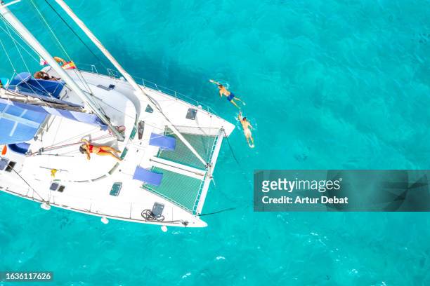 directly above view of a group of friends swimming in the water sailing with catamaran on the formentera island in spain. - catamaran sailing stock pictures, royalty-free photos & images