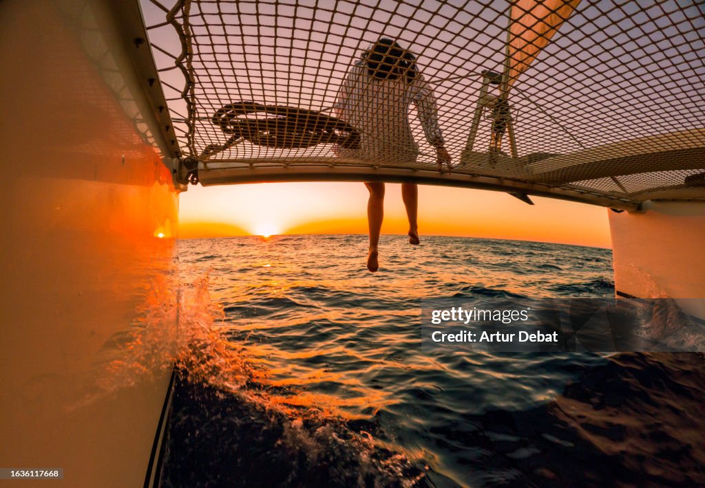 Creative angle of a woman sitting on the catamaran bow contemplating the sea while sailing during the sunset in Spain.