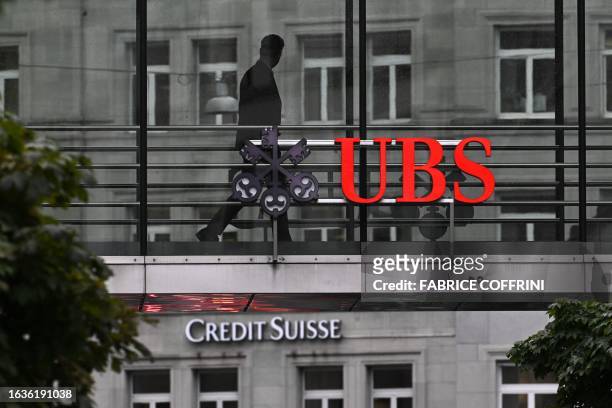 An employee of UBS walks past a sign of Swiss giant banking above a sign of Credit Suisse on August 31, 2023 in Zurich, after the announcement by UBS...