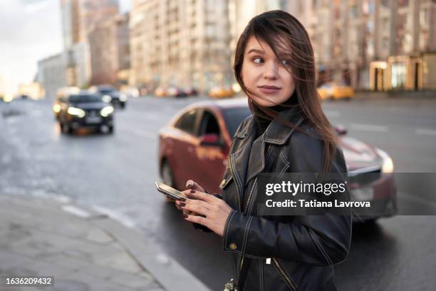 attractive young female millennial generation in the street. portrait of a woman waiting for a taxi on a windy autumn day. lifestyle photo with copy space - air taxi stock pictures, royalty-free photos & images