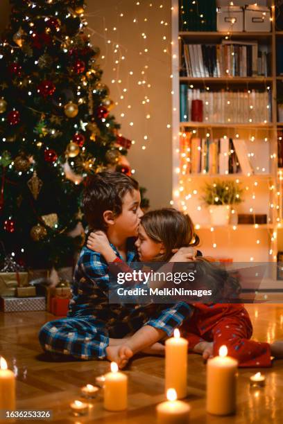 children bonding and embrace in front of christmas tree at home - hug christmas stock pictures, royalty-free photos & images