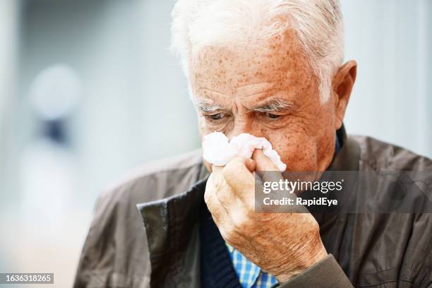 anciano sonándose la nariz en un pañuelo en la calle: tiene un resfriado o gripe - sonarse fotografías e imágenes de stock