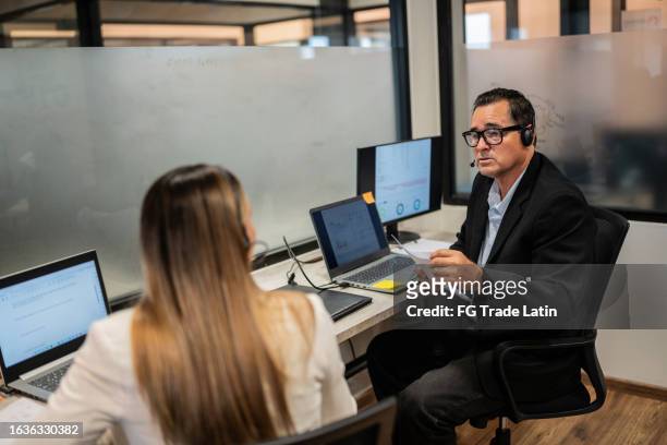 reifer mann, der mit seinem kollegen spricht, während er im büro arbeitet - halb mann halb frau stock-fotos und bilder