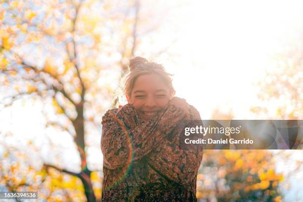 girl in an autumn dress looking at the camera and surrounded by an autumnal atmosphere, smile facing the autumnal cold - setembro imagens e fotografias de stock