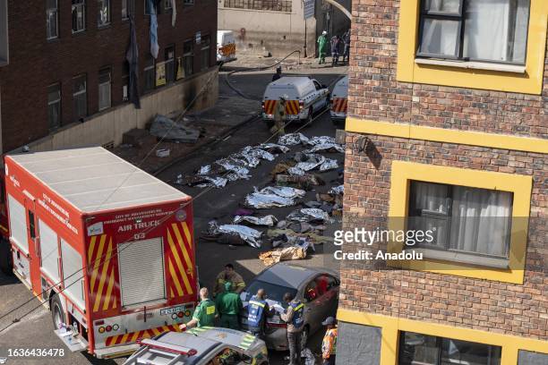 Firefighters and healthcare professionals are deployed at the scene as bodies covered in blankets and sheets are seen after fire at a five-story...