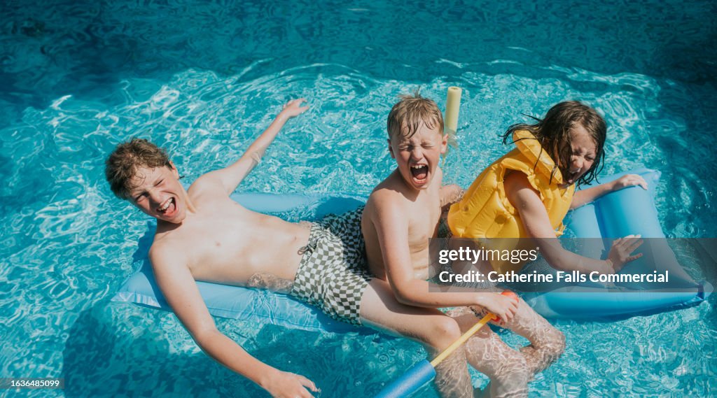 Three siblings sit on a pool float - they squeal with delight
