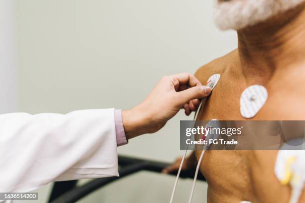 close-up of doctor hands putting sensors of electrocardiography on a doctor's office - stress test stock pictures, royalty-free photos & images