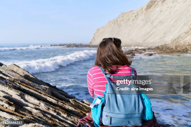 rear view of adult woman looking away sitting on trunk in the sunset at beach - female looking away from camera serious thinking outside natural stock pictures, royalty-free photos & images