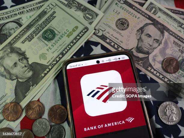In this photo illustration, Bank of America Corporation logo is seen displayed on a smartphone and US currency notes and coins in the background.