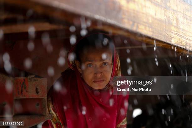 Woman takes shelter under a cargo vehicle during rainfall in Dhaka, Bangladesh on August 31, 2023.