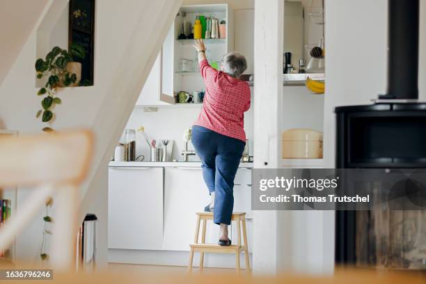 Symbolic photo on the topic of accident risk in the household. An old woman is standing on a stool in a kitchen on August 31, 2023 in Berlin, Germany.