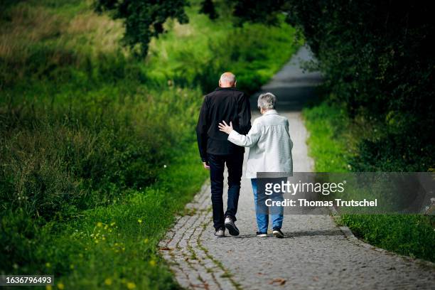 Symbolic photo on the subject of pensioners. An old married couple is walking along a path together, with the wife supporting her husband on August...