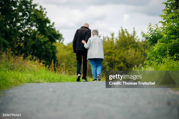 Symbolic photo on the subject of pensioners. An old married couple is walking along a path together, with the wife supporting her husband on August...