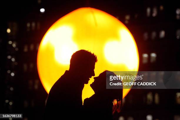 Couple pose for pictures against the backdrop of a 'fake sun' in London's Trafalgar Square, on January 23, 2012. The luminous orb took six months to...