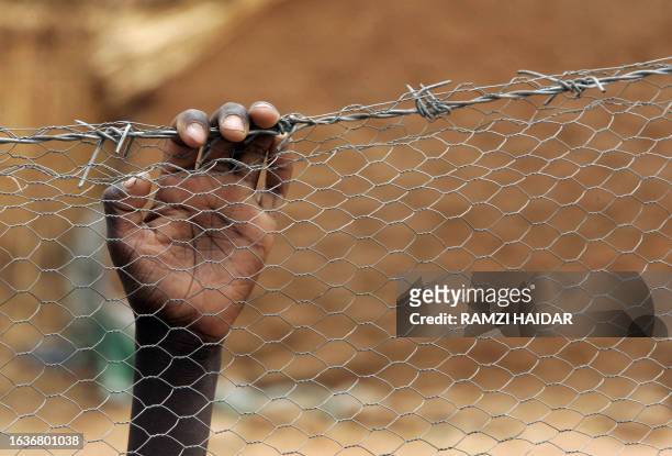 Child's hand grasps barbed wire at Abu Shouk camp, located 7km north-west of Al-Fasher, the capital of North Darfur, 17 May 2006. Abu Shouk is the...