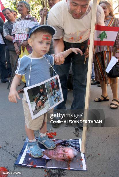 Man holds a kid as he dirties a picture of US President George W. Bush during a protest rally against the Israeli offensive in Lebanon, near the US...