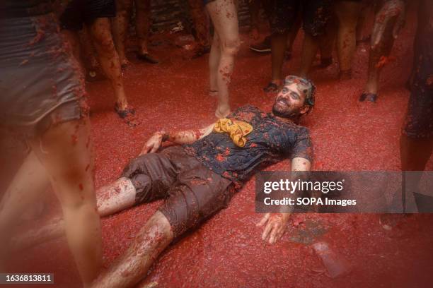 Man covered with crushed tomatoes lies on the ground during the Tomatina festival. Every last Wednesday of August, La Tomatina is celebrated in the...