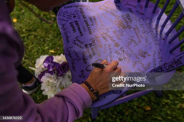 August 31, 2023: A woman writes a message on a purple chair in memory of those lost to drug overdoses as many Edmontonians gathered at Victoria Park...