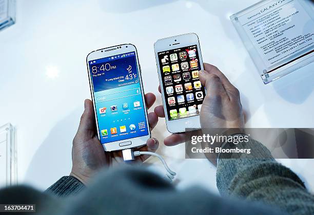 An attendee holds a Samsung Electronics Co. Galaxy S4 smartphone, left, next to an Apple Inc. IPhone 5 during an event at Radio City Music Hall in...