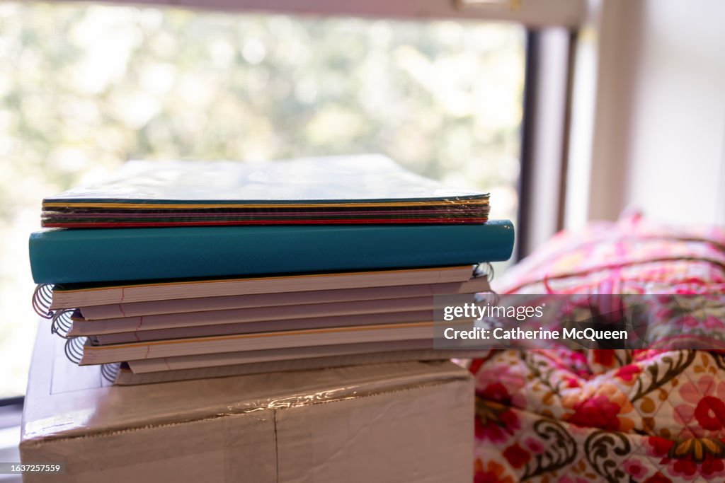 Stack of notebooks & folders, box & duffel bag on desk in student dorm room