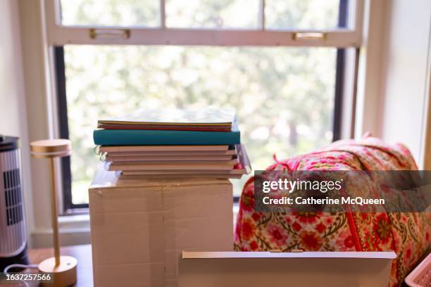 stack of notebooks & folders, boxes, duffel bag, lamp & fan on desk in student dorm room - gateway high school stock pictures, royalty-free photos & images