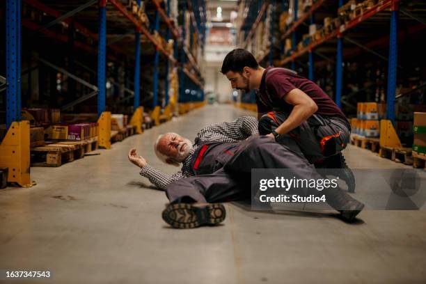 a painful manual worker lying down injured at the warehouse while his colleague is helping him. - trabajador manual stock pictures, royalty-free photos & images