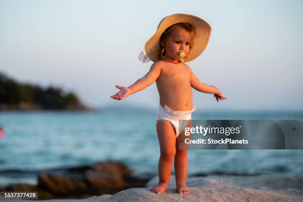 cute baby girl standing on the rock at the beach - pacifier stockfoto's en -beelden