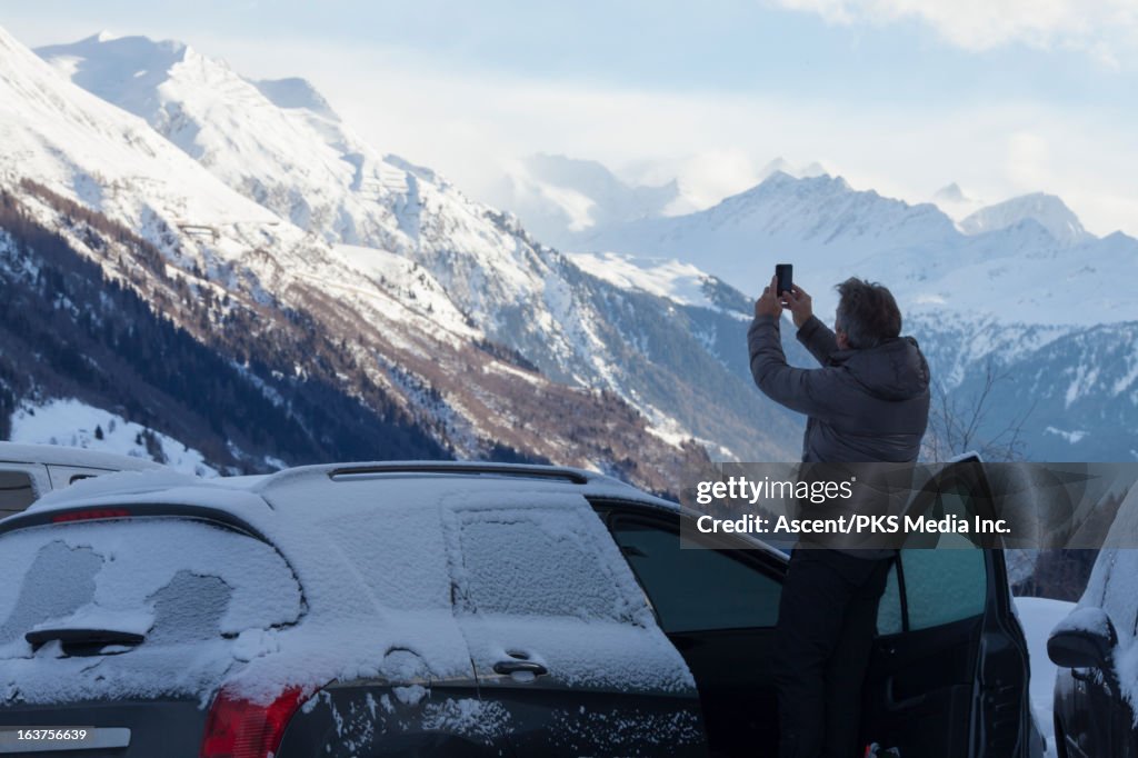 Man takes picture of mtns from snowy car door