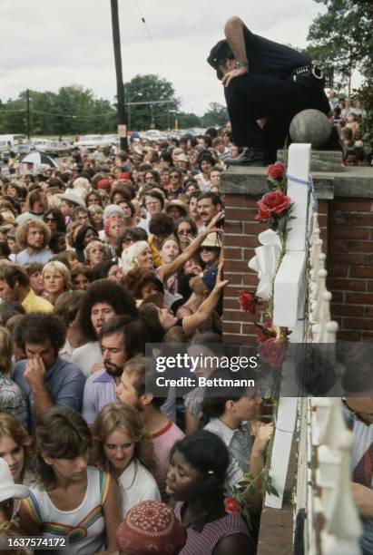Policeman atop a wall keeps an eye on the crowd outside the gates to Elvis Presley's Graceland home following the singer's death in Memphis,...