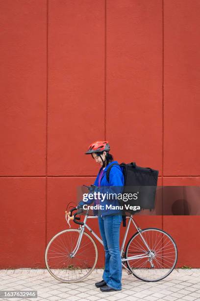 delivery woman using mobile phone while standing outdoors with bicycle. - fahrradkurier stock-fotos und bilder