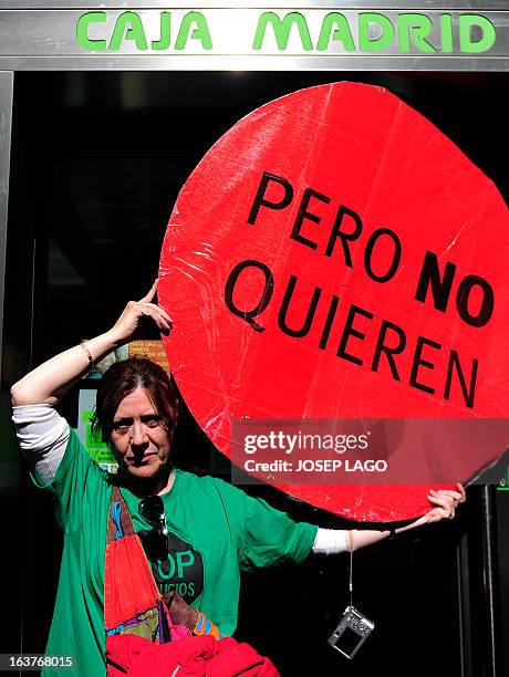 Woman holds a placard reading "because they don't want" as she stands in front of a Caja Madrid bank succursal during a protest by Platform for...