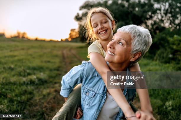 abuela cargando a su nieta en la espalda al aire libre - vida activa fotografías e imágenes de stock