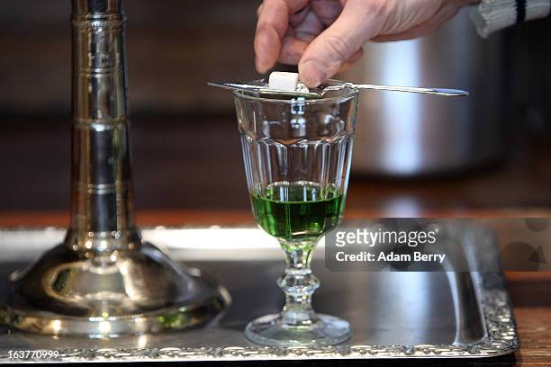 Martial Philippi, owner of the Absinth Depot shop, places a sugar cube onto an absinthe spoon atop a glass of absinthe on March 15, 2013 in Berlin,...